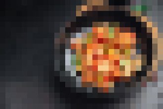 Top-down view of a round skillet or pan containing a colorful, saucy dish with orange, red, and yellow tones; the image is highly pixelated and details are unclear.