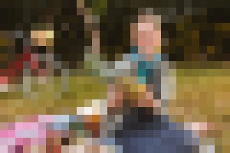 Blurred outdoor scene with a person in the foreground; the background is indistinct due to pixelation, suggesting a daytime social setting.