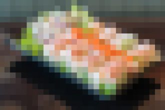 Colorful sushi platter on a dark plate, lightly blurred by pixelation.