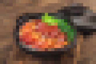 Skillet on a wooden surface filled with colorful cooked vegetables in sauce, garnished with a green herb.