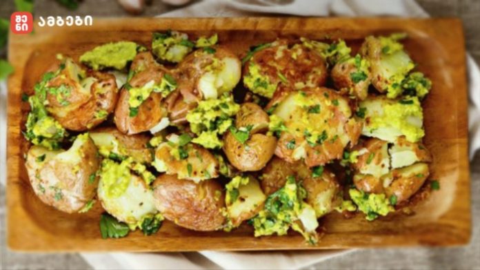 Roasted potato halves on a wooden tray, tossed with chopped parsley and a yellow-green herb sauce.