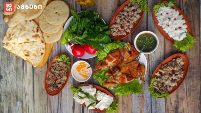 Platters of grilled meat, flatbreads, and fresh vegetables arranged on a wooden table with dips and greens.