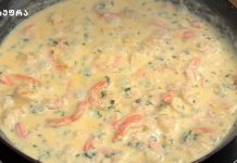 კრევეტები ნივრის და ნაღების სოუსში Creamy sauce simmering in a frying pan with pink strips and chopped herbs.