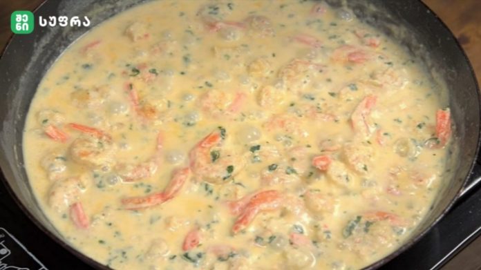 Creamy sauce simmering in a frying pan with pink strips and chopped herbs.