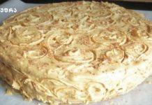 დესერტი შესქელებული რძით Round vanilla cake with white buttercream frosting and decorative swirl rosettes on top, sides covered in creamy frosting curls, placed on parchment paper.