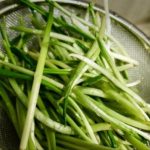 Fresh scallions (green onions) sliced into thin strips in a metal colander.