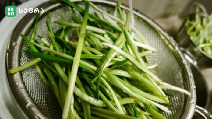 Fresh scallions (green onions) sliced into thin strips in a metal colander.