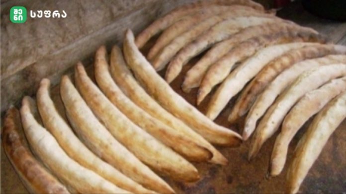 Rows of curved bread sticks cooling on a rustic baking sheet, with more sticks stacked in the background.