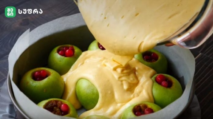 Green apples hollowed and arranged in a round cake pan, batter being poured over them for baking.