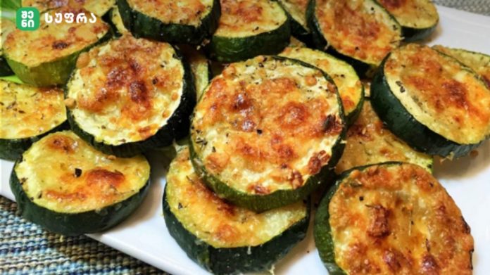 Plate of baked zucchini rounds topped with melted golden cheese and herbs on a white platter