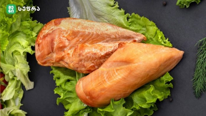 Two raw salmon fillets resting on a bed of lettuce leaves on a dark surface with herbs nearby
