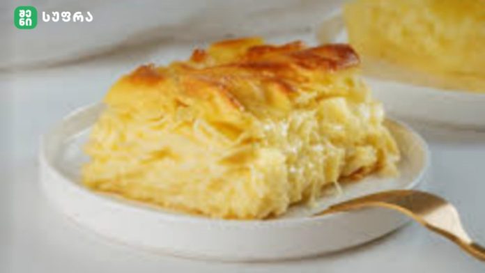 Golden, flaky cheesy pastry slice on a white plate with a gold spoon beside it.