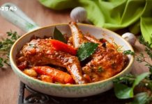 Მოამზადეთ ოჯახური ბერძნულად Skillet with braised meat and carrots in tomato sauce, garnished with bay leaves and herbs on a wooden table.