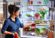 რომელი ხილისა და ბოსტნეულის შენახვა არ შეიძლება მაცივარში და რატომ? Woman in a blue shirt standing by an open refrigerator, selecting a red bell pepper from fresh vegetables inside.