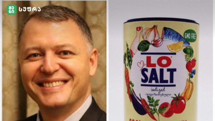 Smiling man in a suit on the left beside a colorful LO SALT iodized salt can on the right, with fruit and vegetable illustrations.