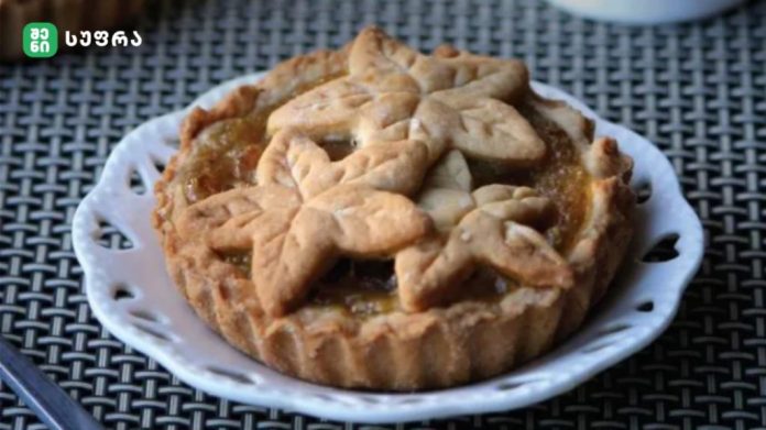 Pie topped with leaf-shaped crust lattice on a white plate, set on a woven table.