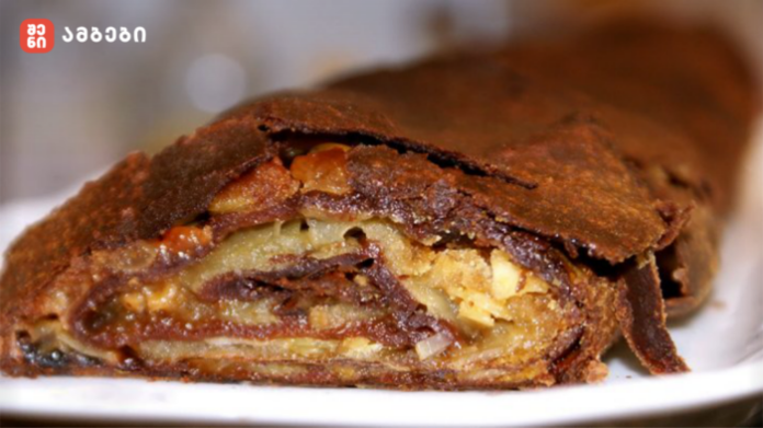 Cross-section of a flaky, chocolate-covered pastry filled with chopped nuts.