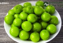 ტყემალი და ალუჩა – მათი სარგებელის შესახებ რა უნდა ვიცოდეთ White bowl overflowing with glossy bright green plums on a dark wooden surface.