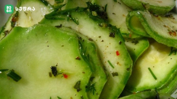 Close-up of thin cucumber slices tossed with chopped dill and herbs, seasoned with red pepper and spices.