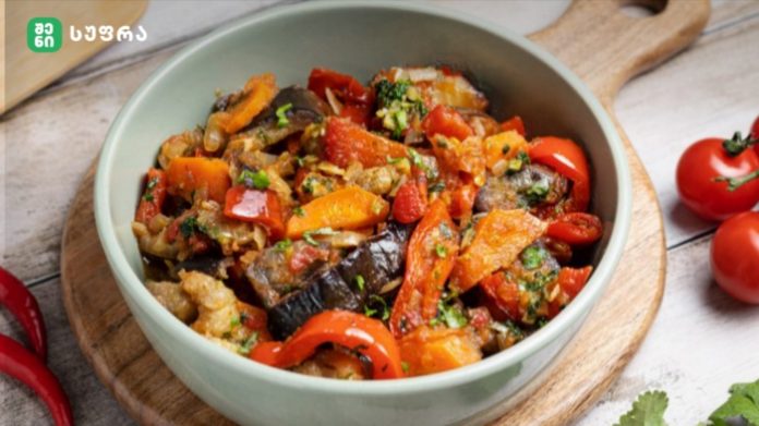 Colorful vegetable medley in a light green bowl: eggplant, red peppers, carrots, and tomatoes with herbs on a wooden board.