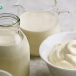 Milk display: glass bottle and small jug of milk with a bowl of whipped cream on a light kitchen surface.