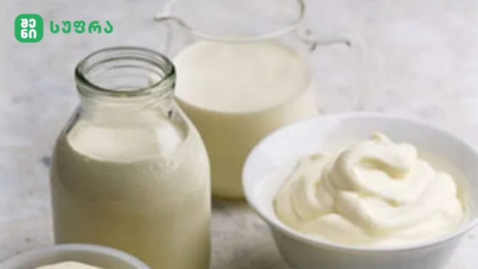 Milk display: glass bottle and small jug of milk with a bowl of whipped cream on a light kitchen surface.