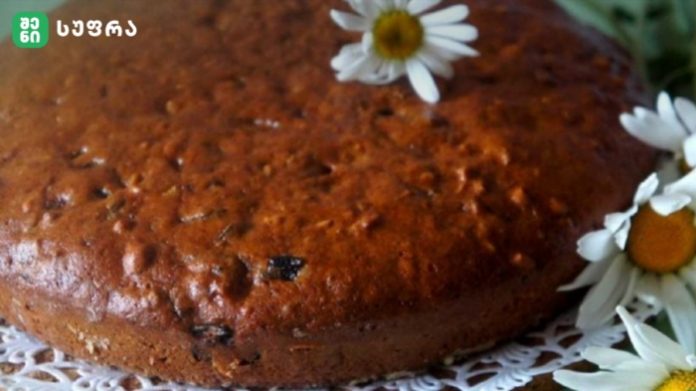 Close-up of a round brown loaf cake on a lace doily, with white daisies arranged around it.