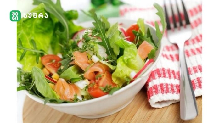 Fresh green salad with smoked salmon, tomatoes and herbs in a white bowl on a wooden table.