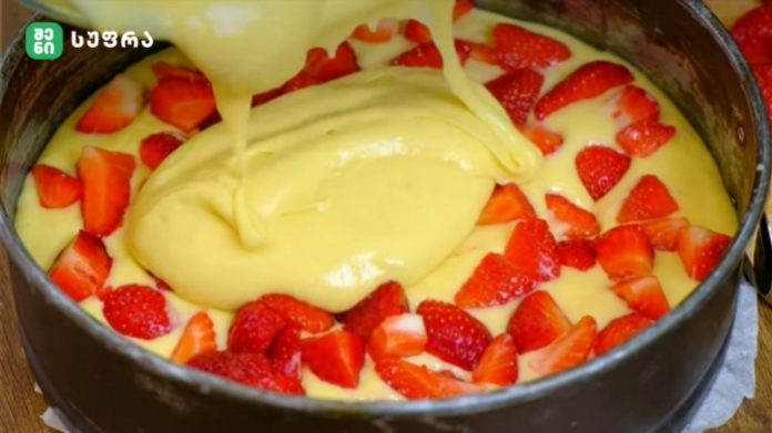 marwyvis namcxvari Round springform pan with yellow batter being poured over fresh strawberry pieces arranged around the edges.
