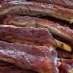 Stack of glazed barbecue ribs with a reddish-brown crust, close-up view.] ,