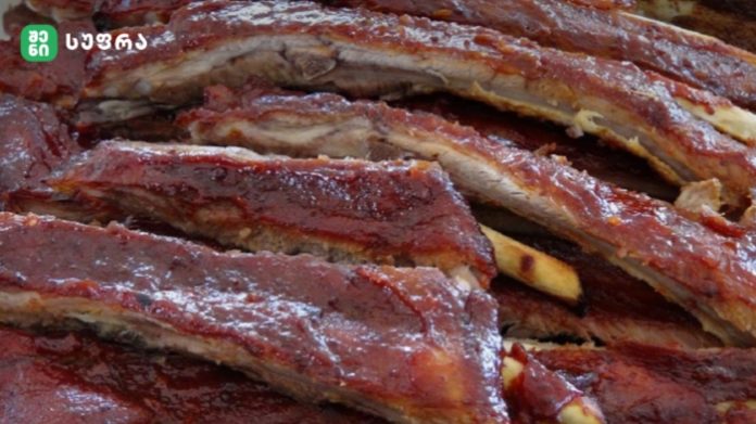 Stack of glazed barbecue ribs with a reddish-brown crust, close-up view.] ,
