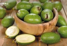 ფეიხოა -ძალიან სასარგებლო ხილი Green feijoa fruits in a wooden bowl on a wooden surface, with a couple cut open to show pale flesh inside.