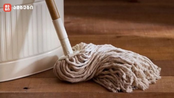 Beige mop head wringing on a wooden floor beside a white bucket.