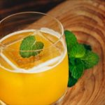 Glass of orange juice with a fresh mint leaf garnish on a wooden board surface