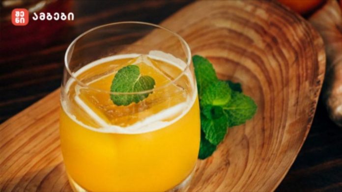 Glass of orange juice with a fresh mint leaf garnish on a wooden board surface