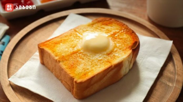 Square slice of toasted bread with a knob of butter melting on top, placed on a white napkin on a wooden plate.