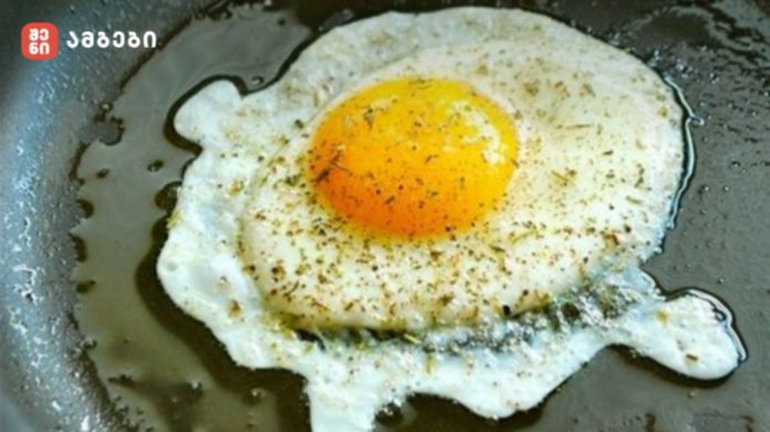 Sunny-side-up egg frying in a skillet, with a small logo in the upper-left corner.