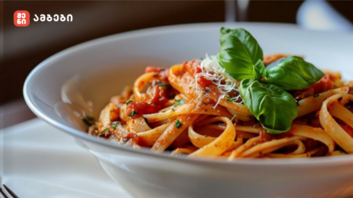 Bowl of spaghetti with tomato sauce, grated cheese, and fresh basil on top, in a white dish.