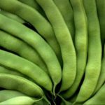 Pile of fresh green beans filling the frame, with a red logo in the top-left corner.