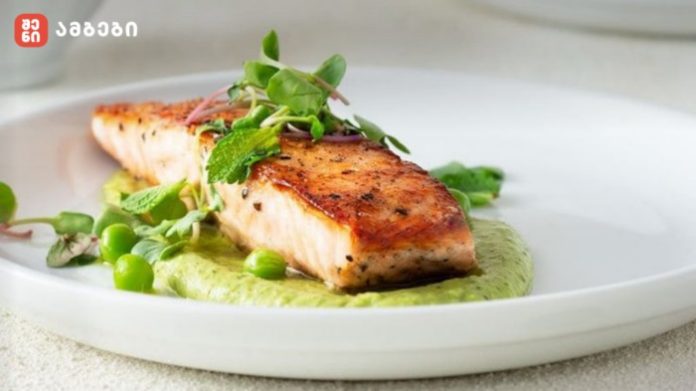 Pan-seared salmon fillet on a bed of green herb sauce with peas and microgreens on a white plate