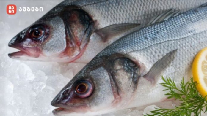 Two fresh whole fish on crushed ice with a lemon slice and dill garnish in a display.