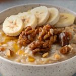Bowl of oatmeal topped with banana slices and walnuts, with a drizzle of honey.