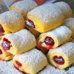 Plate of powdered-sugar dusted cherry-filled rolled pastries stacked in a pyramid on a decorative plate