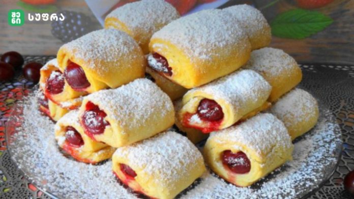 Plate of powdered-sugar dusted cherry-filled rolled pastries stacked in a pyramid on a decorative plate