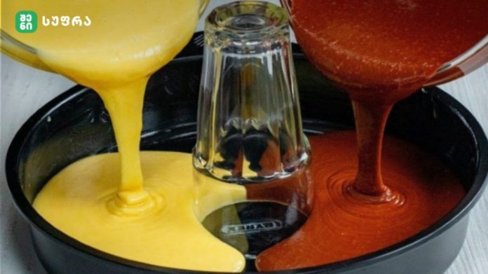shenisupra-keqsi-2-1024x575 Bright yellow and red cake batters pour into a round baking tin, with a glass bottle centered in the pan between the two streams.
