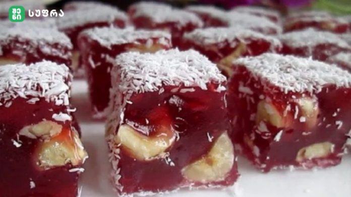Red jelly dessert squares with banana chunks and a coconut flake topping, close-up view.