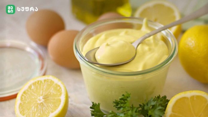 Creamy lemon curd in a glass jar with a spoon, surrounded by lemons, eggs, and parsley.