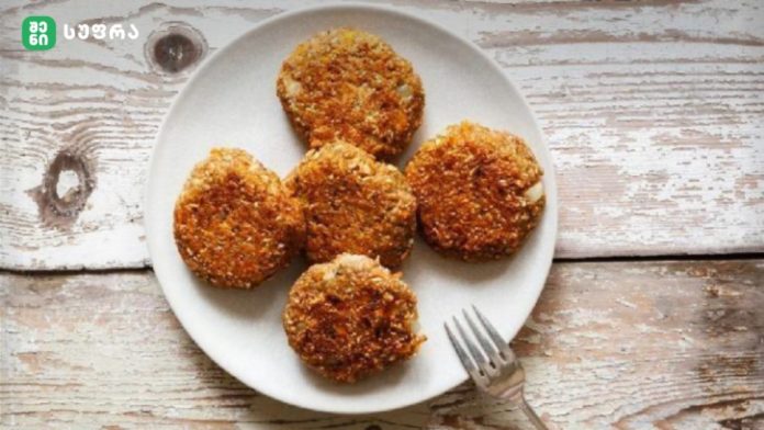 shenisupra-sokos-katleti-1024x576 Five crispy, breaded croquettes arranged on a white plate atop a rustic wooden table, with a fork nearby.