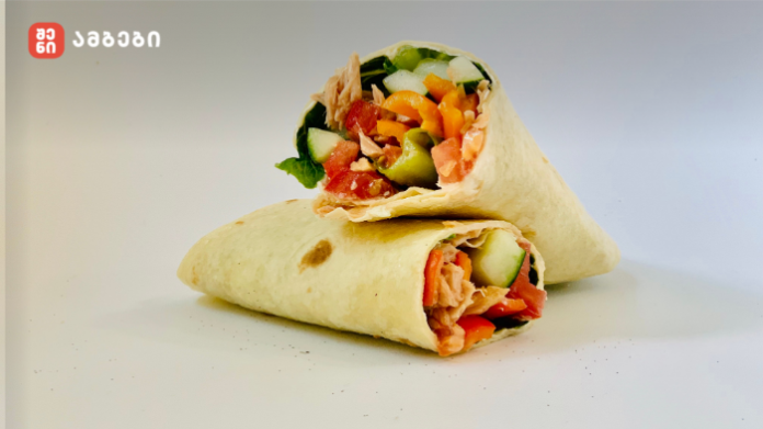 Two soft wraps filled with chicken and fresh veggies, placed on a white surface; logo in the upper-left corner.