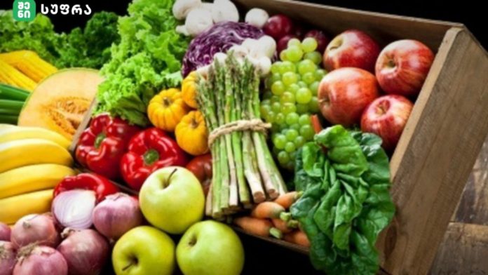 Assorted fresh produce in a wooden crate: apples, bananas, peppers, greens, grapes, carrots, onions, and garlic